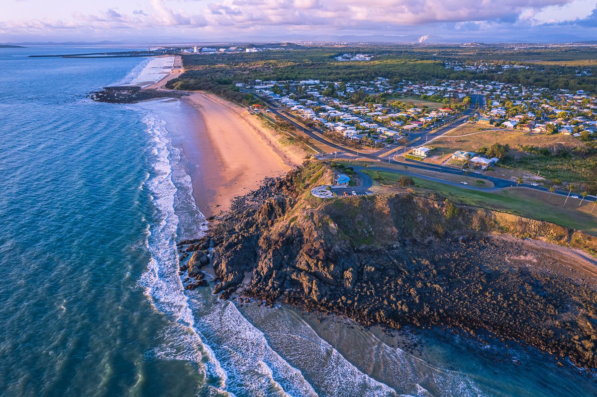 Aerial view of a coastal neighbourhood with pristine beachfront, inviting potential homeowners to 'Open for Inspection' events with a promise of a serene lifestyle